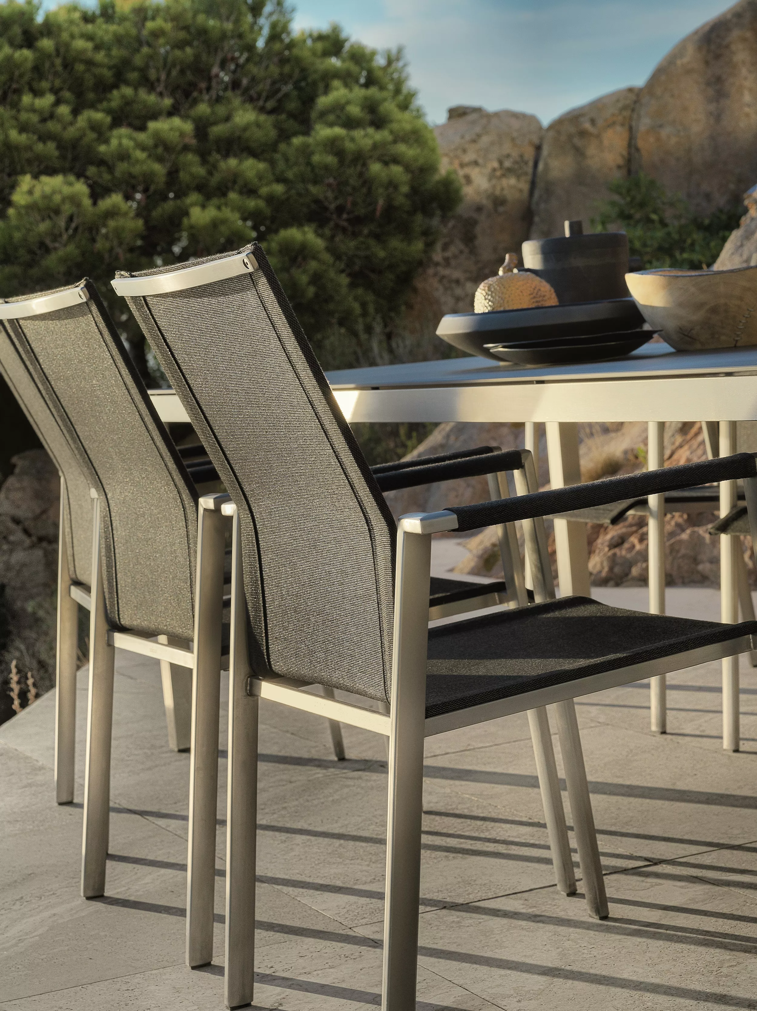 Zwei Solpuri Dance Stühle aus Stahl stehen an einem Tisch im Freien mit Schalen und Dekorationen im Hintergrund.