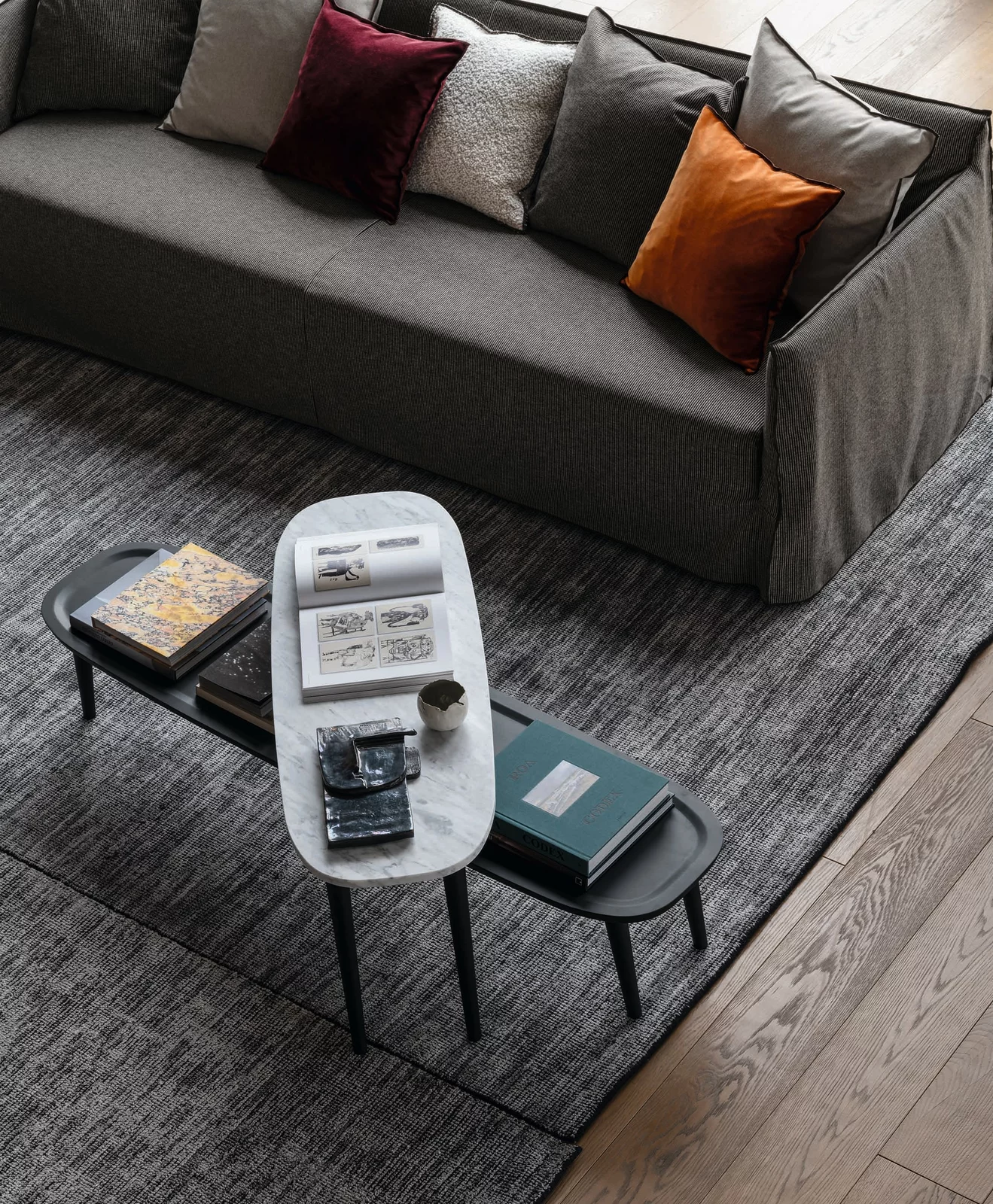 Gervasoni Sofa mit Kissen in verschiedenen Farben und Couchtisch mit Büchern und Zeitschriften auf einem grauen Teppich in einem Wohnzimmer.