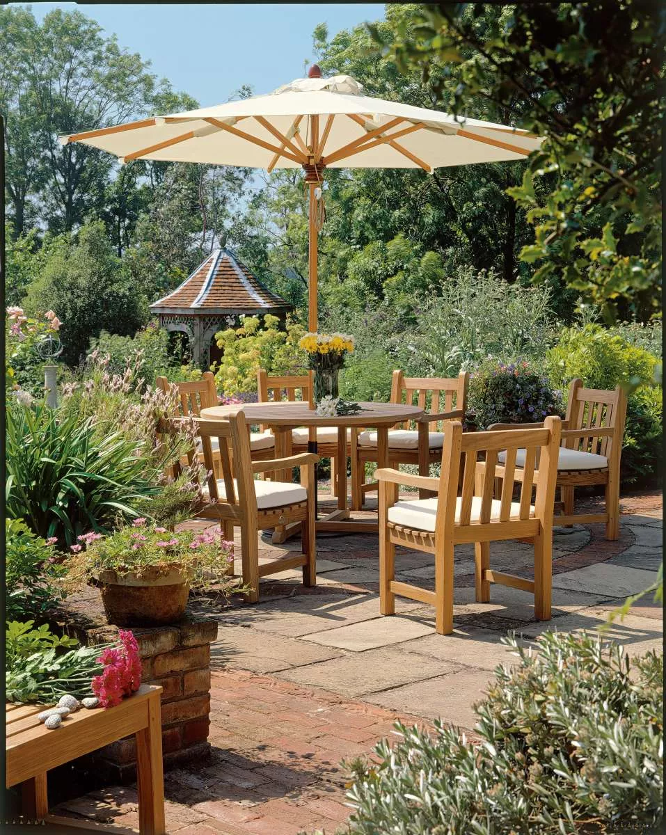 Barlow Tyrie Felsted Bank aus Teakholz, 150 cm, auf einer sonnigen Terrasse mit Gartenmöbeln und Sonnenschirm von Villa Schmidt.