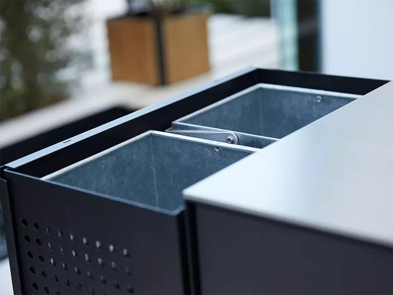 Cane-line Drop Küche in Schwarz, Detailansicht der Metallbehälter, auf einer Terrasse mit unscharfem Hintergrund.