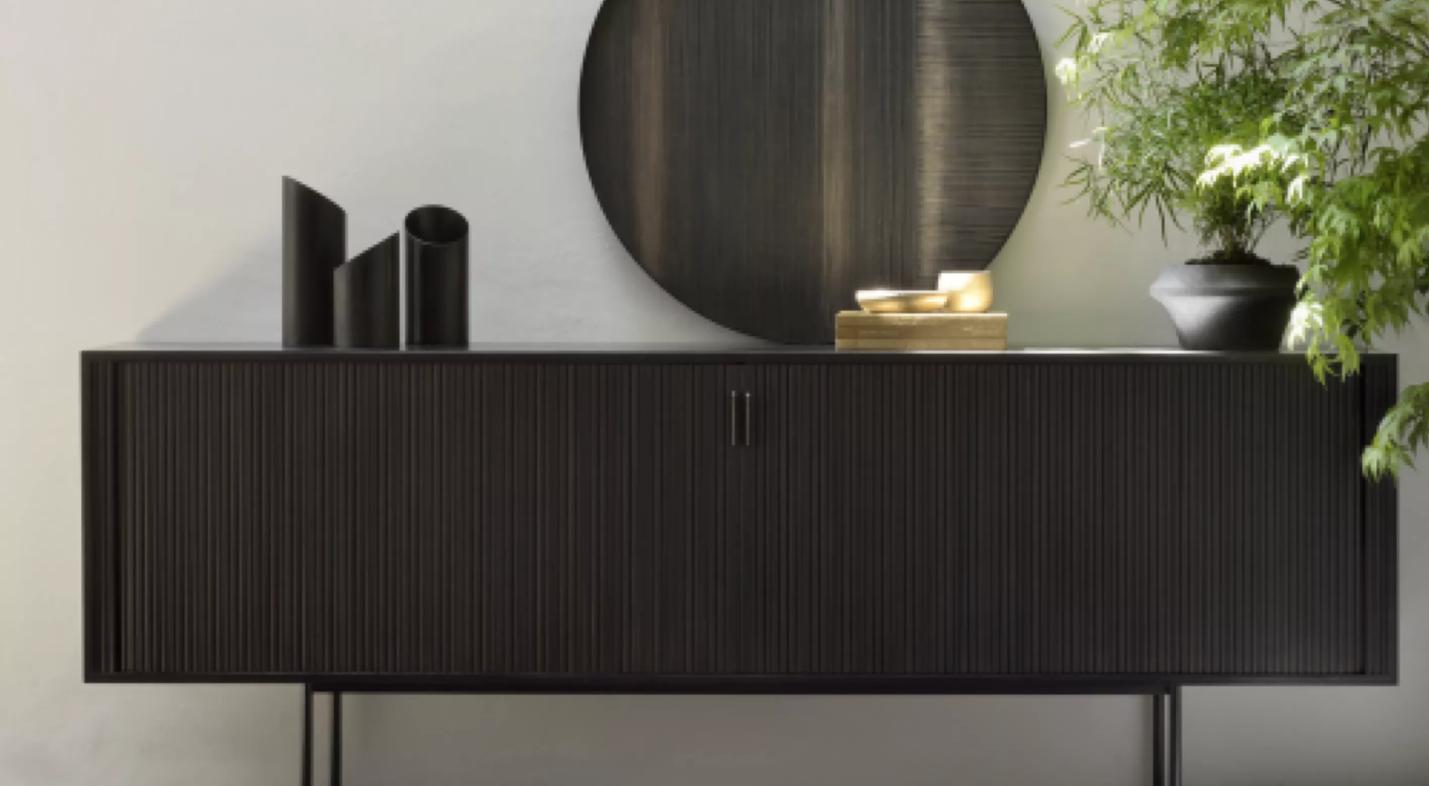 Schwarzes Sideboard von Villa Schmidt vor einer hellen Wand mit runder Spiegeldekoration und grüner Pflanze im Hintergrund.