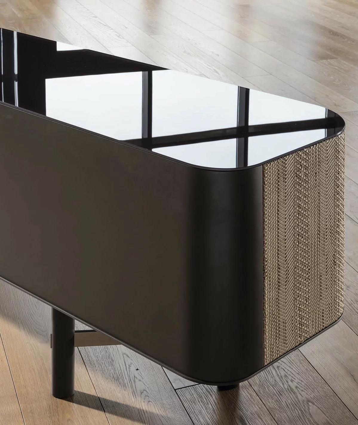 Gervasoni Beistelltisch mit schwarzer Glasplatte und geflochtenem Seitenteil auf einem Holzboden in einem modernen Raum ohne Hintergrund