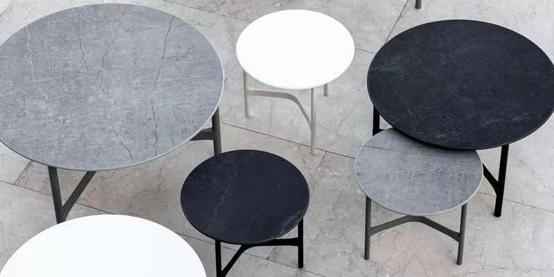 Runde Cane-line Twist Tische in Grau, Schwarz und Weiß auf hellem Steinboden aus der Vogelperspektive.