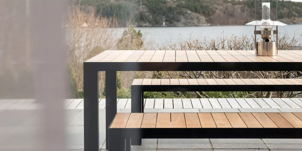 Roshults Gartenmöbel-Kollektion in Naturholz und Metall, auf einer Terrasse mit Seeblick, stimmungsvolles Bild bei Tageslicht.