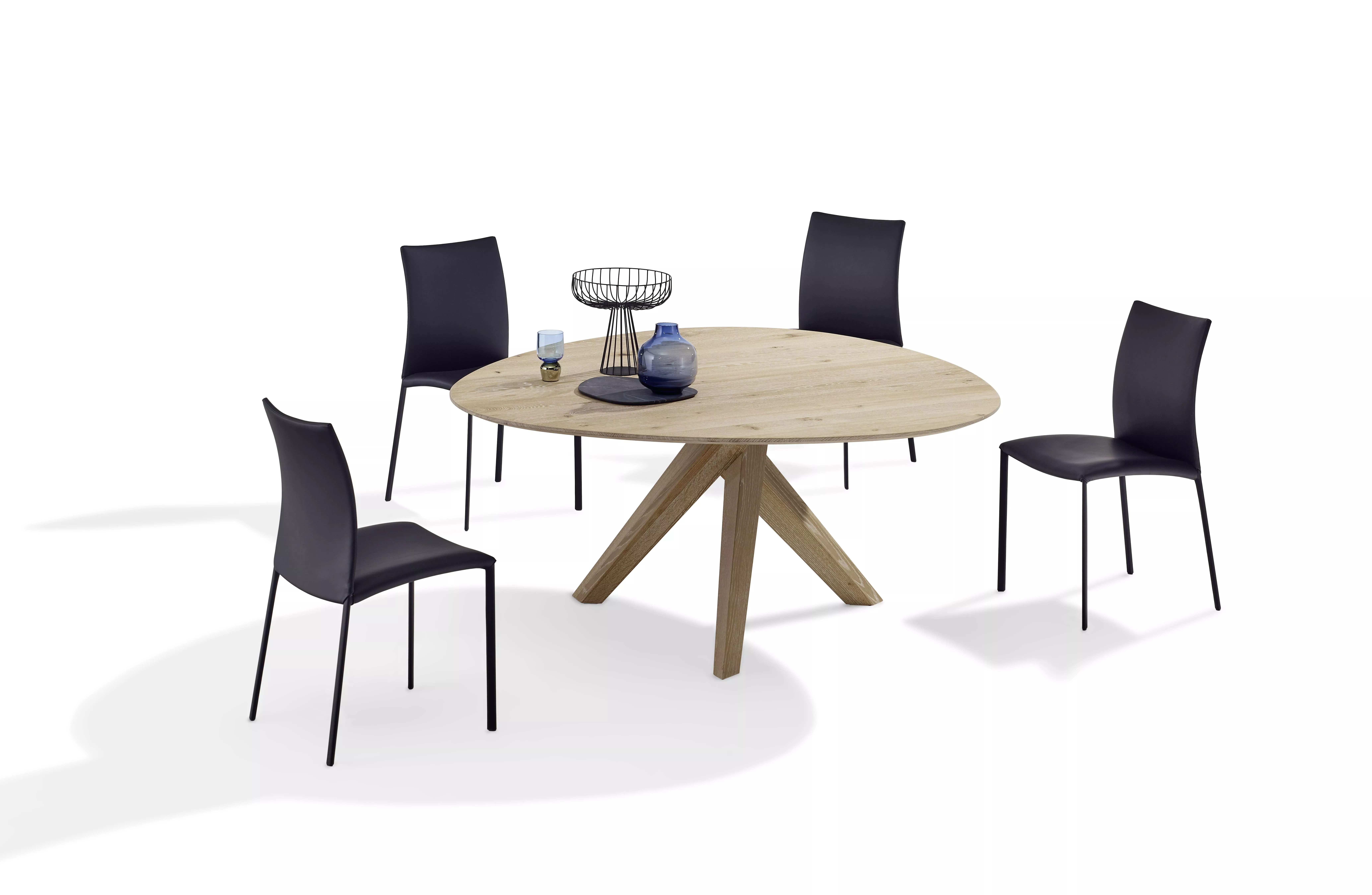 DRAENERT Nobile Soft Esstisch mit runder Holzplatte und vier schwarzen Stühlen auf weißem Hintergrund mit Dekorationen wie Vasen und Schalen