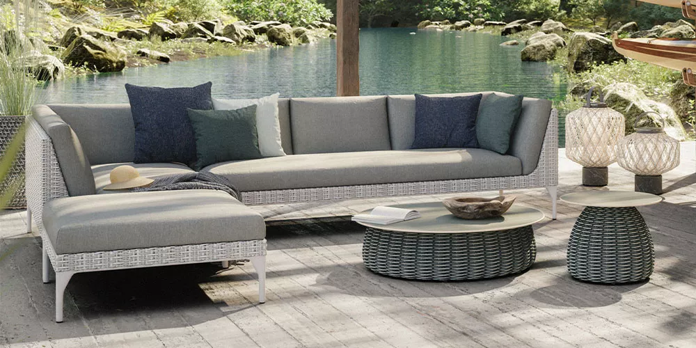 Loungesofa von Villa Schmidt in Grau auf einer Terrasse mit Blick auf einen See, dekoriert mit Kissen und Laternen, stimmungsvolle Atmosphäre.