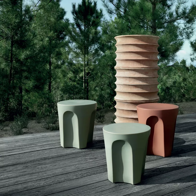 B&B Italia Colosseo Beistelltisch und Hocker in verschiedenen Farben auf einer Holzterrasse im Freien umgeben von Bäumen