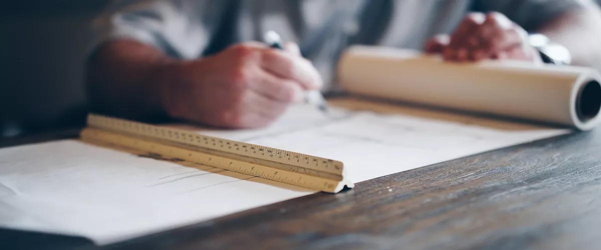 Ein Architekt zeichnet auf einem großen Blatt Papier mit einem Lineal auf einem Holztisch, technische Zeichnung im Büro.