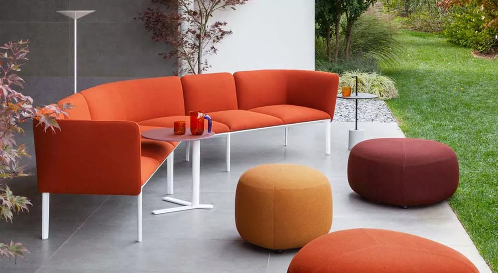 Lapalma ADD Outdoor Loungegruppe in Rot und Orange auf einer Terrasse mit Gartenblick, bestehend aus Sofas und Hockern.