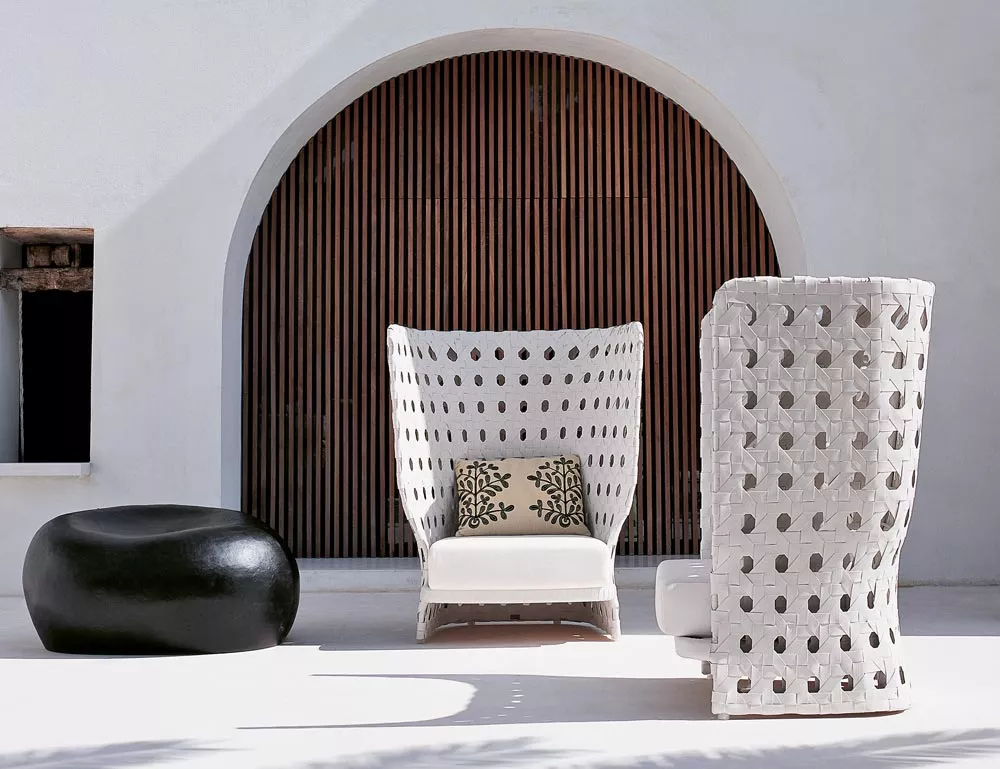 B&B Italia Canasta Outdoor Loungegruppe mit einem Sessel und einem Hocker in einem modernen Außenbereich mit einem schwarzen Pouf und einem Kissen.