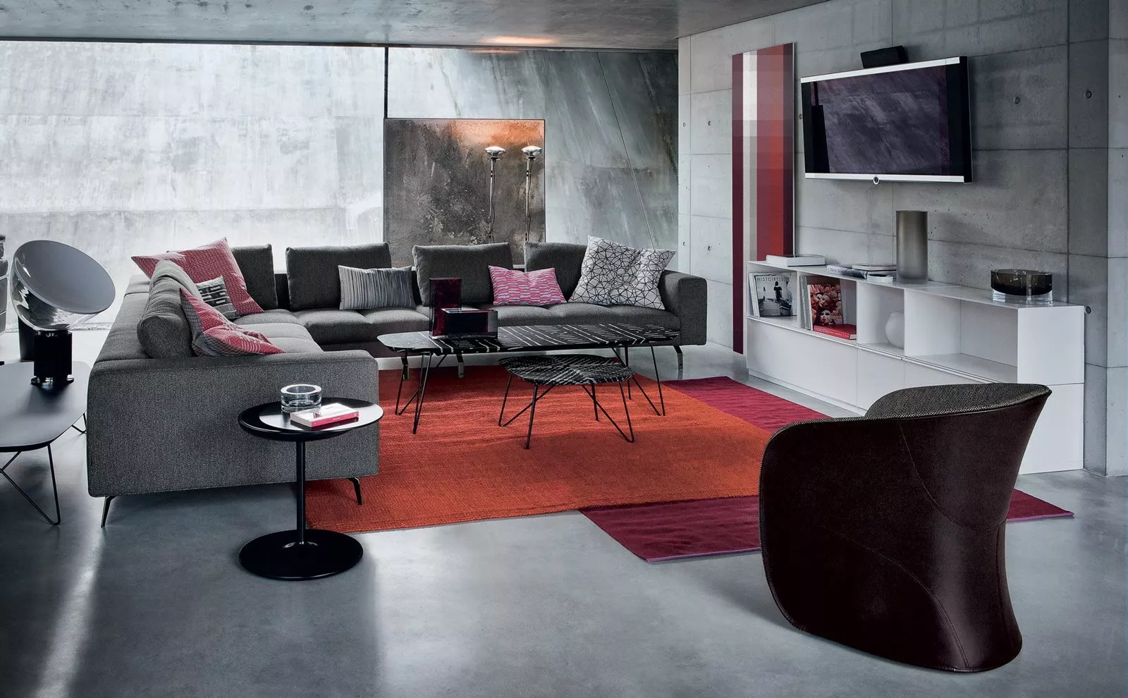 Ein modernes Wohnzimmer mit Zanotta 873 Calla Sofa und stilvollen Möbeln in einem gemütlichen Ambiente mit roten Akzenten und Betonwänden.