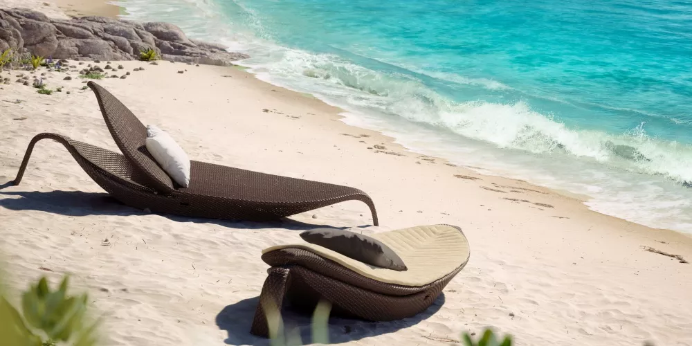 Zwei braune DEDON Leaf Sonnenliegen am Strand mit türkisfarbenem Meer im Hintergrund, entspannte Urlaubsstimmung.