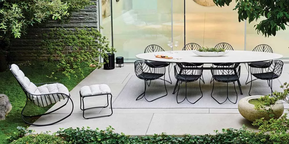 Royal Botania Folia Essgruppe in Schwarz auf einer Terrasse mit grünem Gartenhintergrund, bestehend aus Tisch und Stühlen.