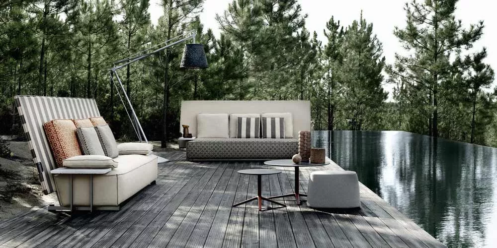 B&B Italia Oh it rains Outdoor Loungegruppe mit Loungesofa und Beistelltischen auf einer Holzterrasse am Pool umgeben von Bäumen