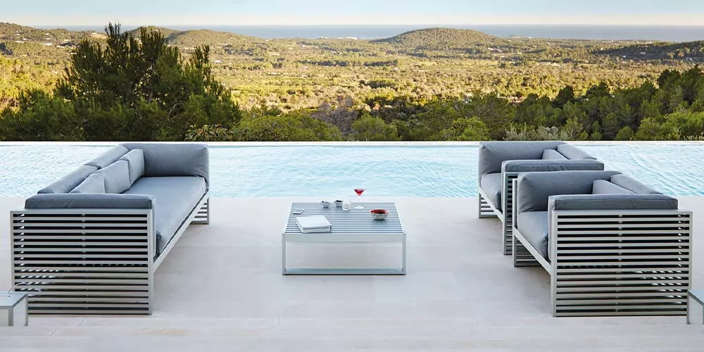 Gandia Blasco DNA Outdoor-Sofa-Set in Grau auf einer Terrasse mit Pool und Blick auf eine hügelige Landschaft im Hintergrund.