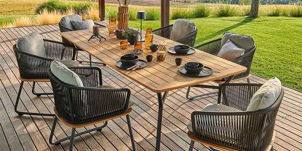 Weishäupl Denia Esstisch-Set in Naturholzoptik mit schwarzen Stühlen auf einer Terrasse mit Blick auf einen grünen Garten.