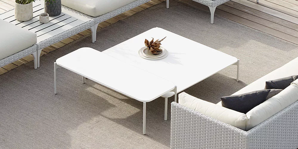 Dedon Kollektion Izon zeigt eine stilvolle Outdoor-Sitzgruppe mit weißen Tischen und bequemen Sofas auf einer Terrasse in einer entspannten Atmosphäre