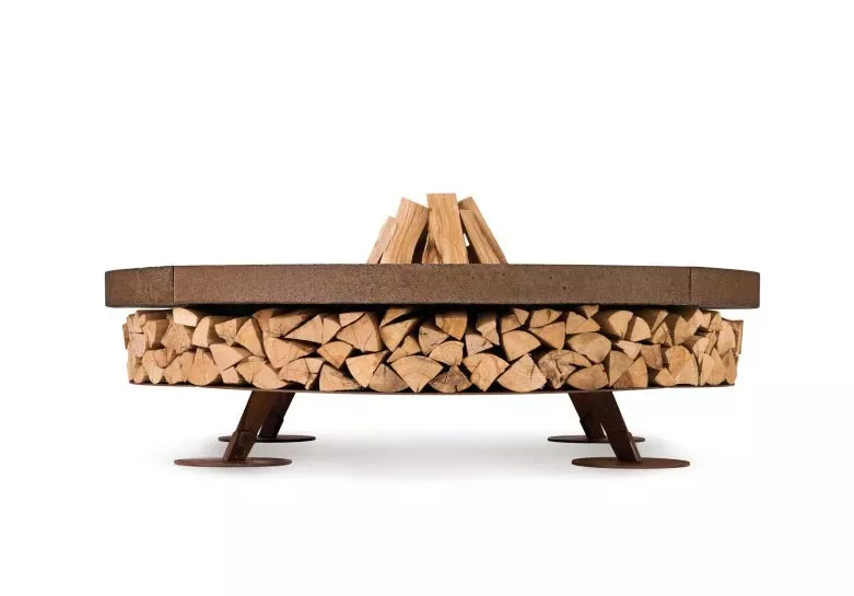 AK47 Ercole Stahl Feuerstelle XSmall 120 cm auf einem weißen Hintergrund mit Holzscheiten darunter gestapelt