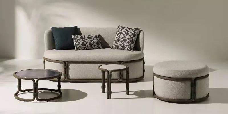 Ethimo Rotin Sofa-Set in Beige mit runden Tischen und Hocker, präsentiert in einem minimalistischen Raum mit neutralem Hintergrund.