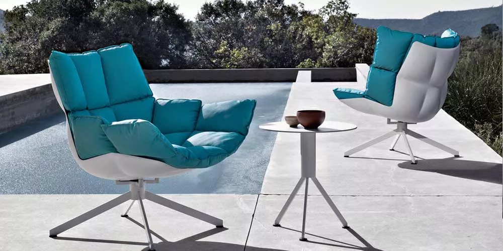 Zwei BeB Italia Husk Outdoor Loungegruppe Stühle in Blau stehen auf einer Terrasse neben einem Pool mit einem kleinen weißen Tisch in der Mitte.