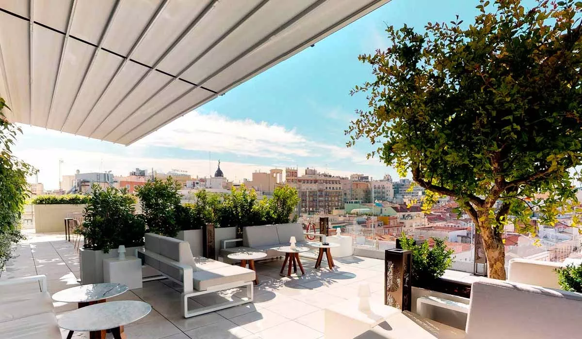 EGO Paris Kama Loungegruppe in Weiß auf einer sonnigen Dachterrasse mit Stadtblick und grünen Pflanzen im Hintergrund.