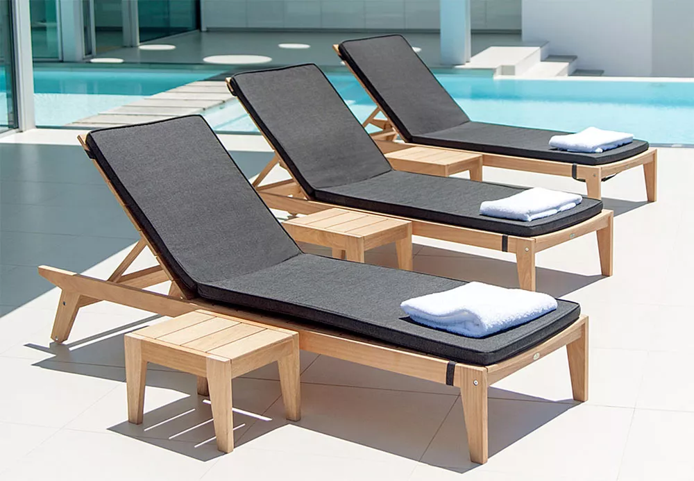 Drei Alexander Rose Roble Sonnenliegen Tivoli in Holzoptik mit grauen Polstern und Handtüchern, auf einer Terrasse am Pool.