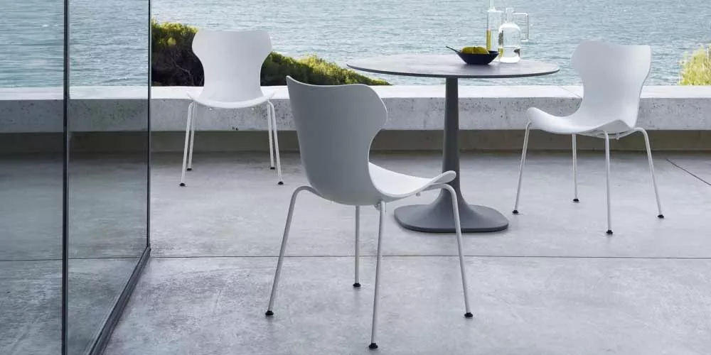 Drei weiße BeB Italia Fiore Outdoor Stühle und ein runder Tisch stehen auf einer Terrasse mit Blick auf das Meer im Hintergrund