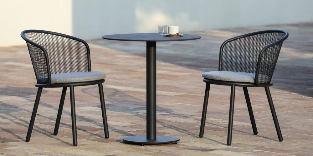 Zwei schwarze Todus Branta Stühle mit grauen Kissen und ein runder Tisch auf einer Terrasse bei Tageslicht.