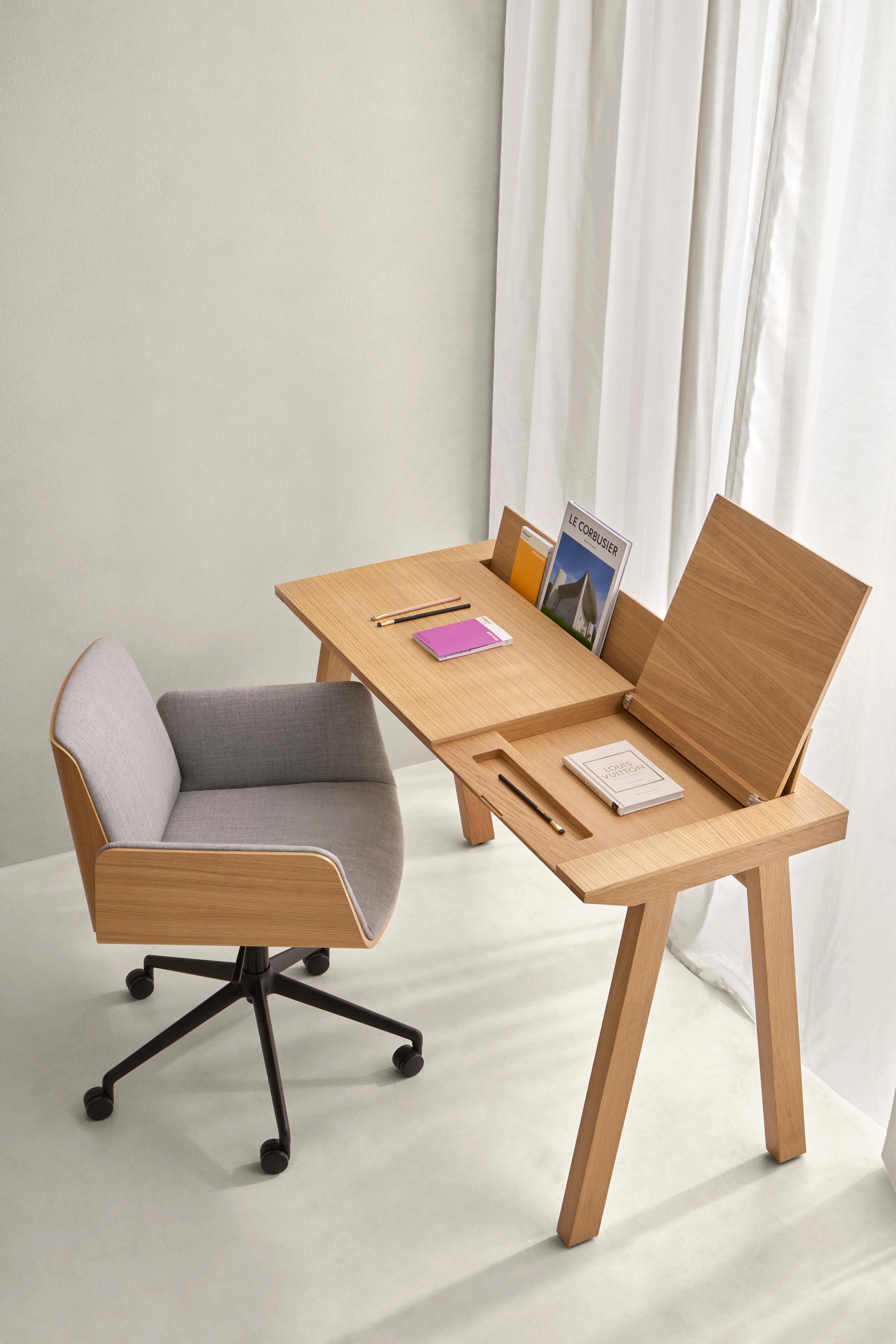 Punt Ernest Schreibtisch in Eiche mit grauem Stuhl, auf hellem Hintergrund, zeigt Bücher und Notizbücher in einer modernen Büroumgebung.