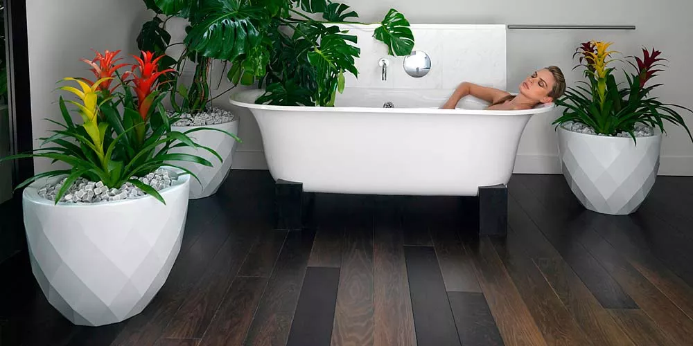 Weiße Vondom Vases Pflanzkübel aus Kunststoff, gefüllt mit bunten Pflanzen, stehen auf dunklem Holzboden neben einer Badewanne.