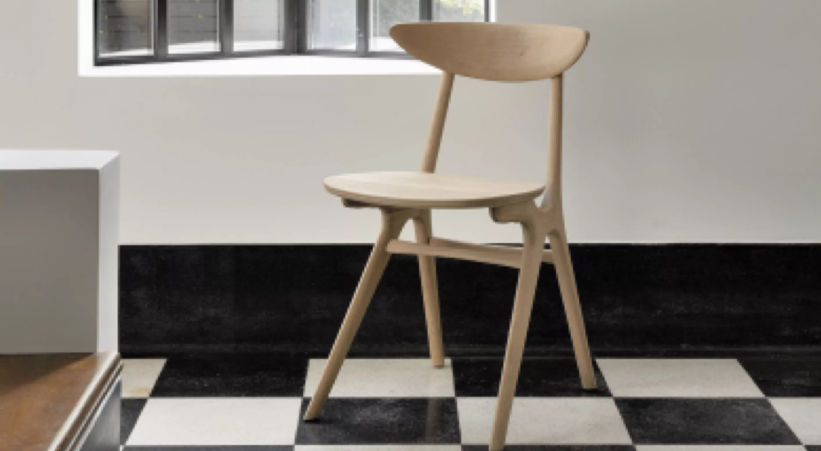 Holzstuhl von Carl Hansen & Søn, Modell CH20, in hellem Naturholz, auf schwarz-weiß kariertem Boden vor einem Fenster.