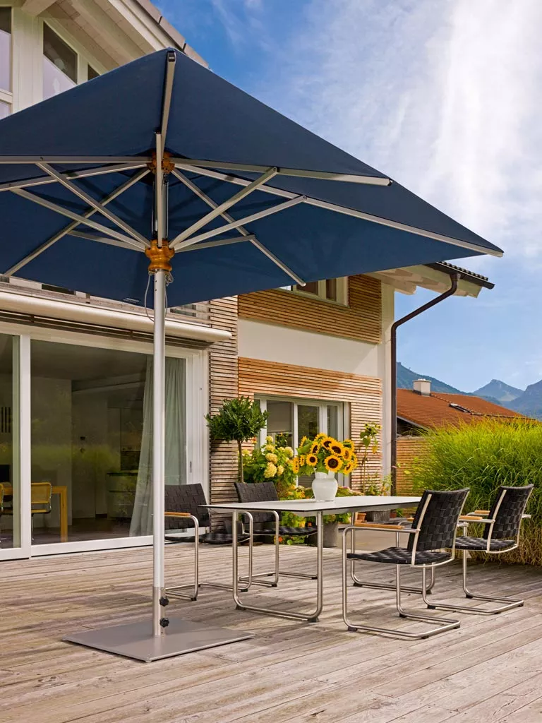 Aluschirm von Weishäupl in Dunkelblau, quadratisch, auf einer Holzterrasse vor einem modernen Haus mit Bergblick im Hintergrund.