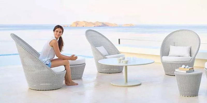Cane-line Kingston Loungegruppe in Grau auf einer Terrasse mit Meerblick, bestehend aus Sesseln, Tisch und Hocker, in entspannter Atmosphäre.