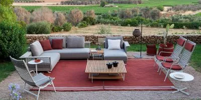 Gartenmöbel-Set Poltrona Frau Solaria in Grau und Rot auf rotem Teppich, umgeben von Natur, mit Blick auf eine Steinmauer und Felder.