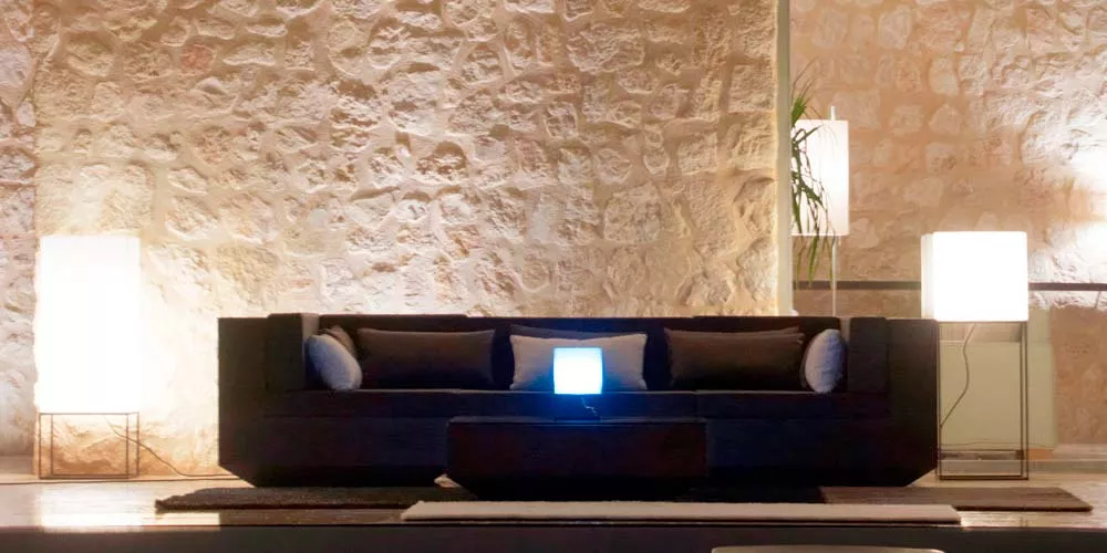 Vondom Vela Leuchten in Weiß, stimmungsvolle Beleuchtung vor einer Steinwand, moderne Atmosphäre im Wohnzimmer.