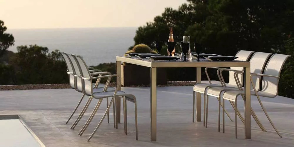 Royal Botania Red Label QT Essgruppe in modernem Design auf einer Terrasse mit Meerblick bei Sonnenuntergang.