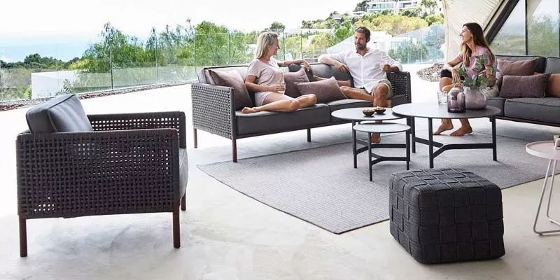 Drei Personen entspannen auf der grauen Cane-line Encore Loungegruppe auf einer Terrasse mit modernem Hintergrund.