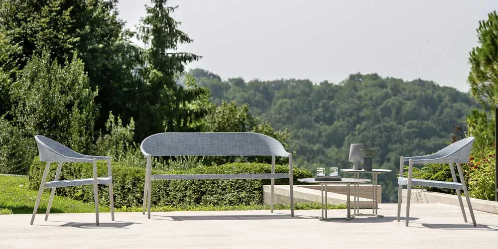 Varaschin Clever Loungegruppe in Grau auf einer Terrasse mit Blick auf grüne Hügel, bestehend aus zwei Sesseln, einem Sofa und einem Tisch.