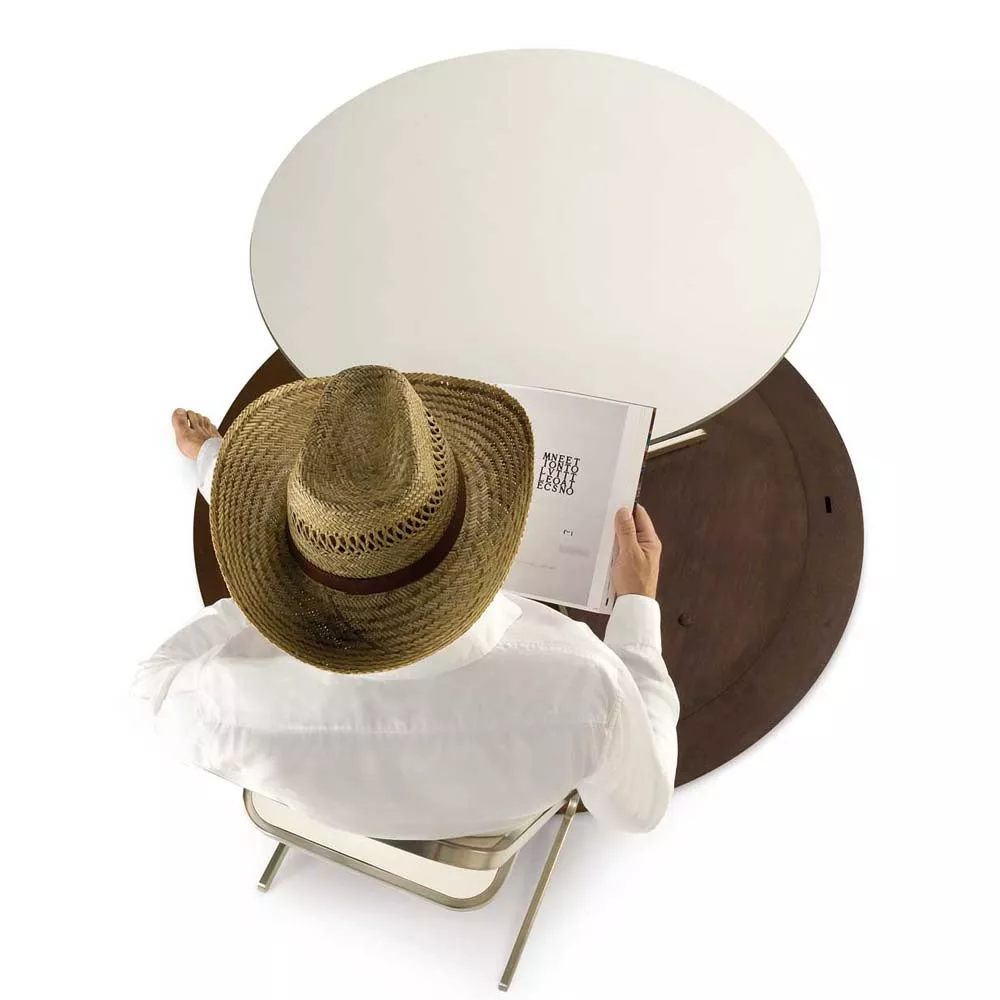 Ein Mann mit Strohhut sitzt auf einem Stuhl und liest ein Buch an einem runden Tisch in einer entspannten Atmosphäre.