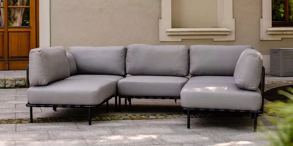 Grau, Royal Mirage Genf Kollektion, Outdoor-Sofa auf einer Terrasse vor einer beigen Hauswand, stimmungsvolles Ambiente.