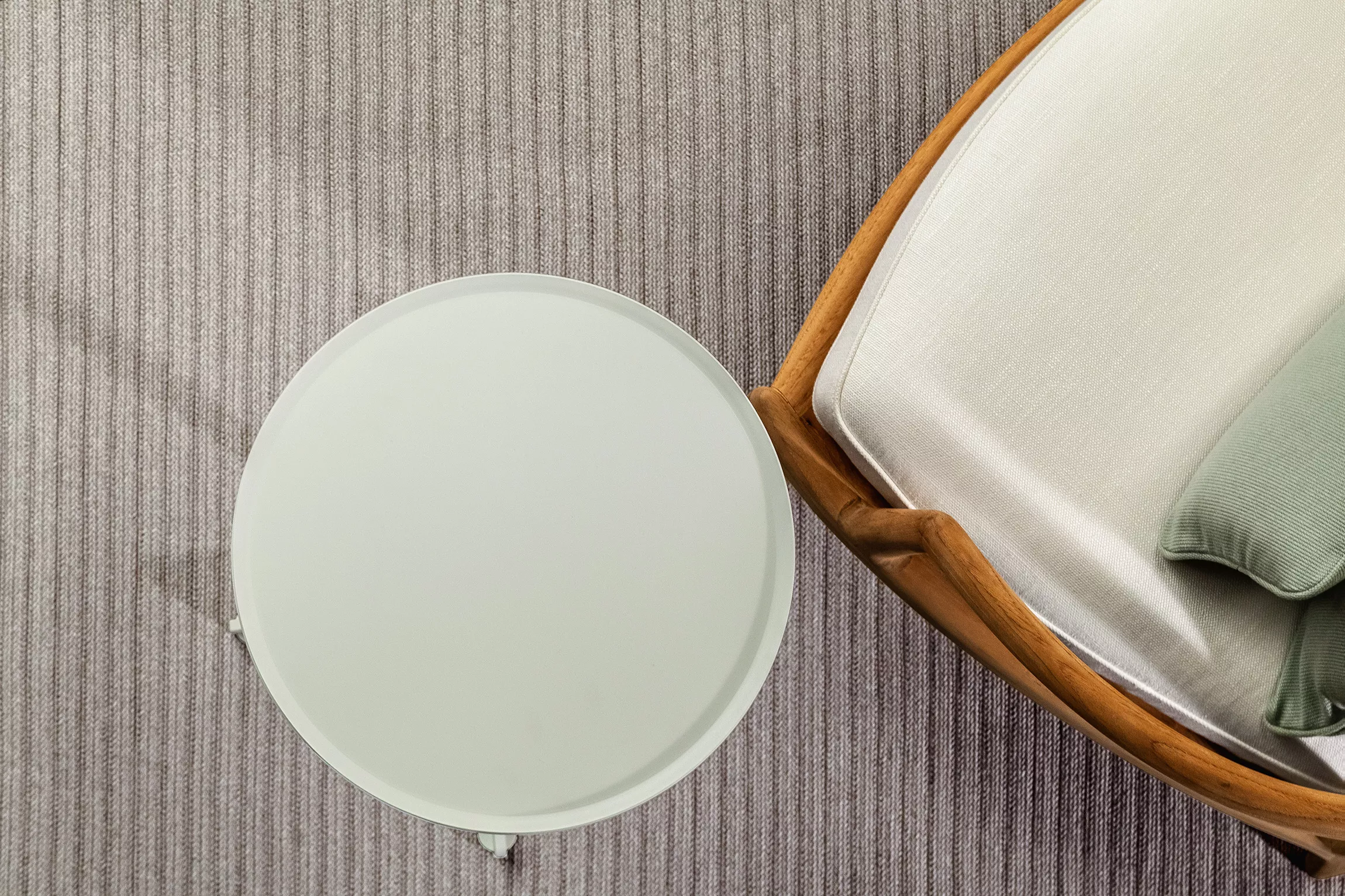 Beistelltisch von Villa Schmidt in Weiß neben einem Holzsessel mit hellen Polstern auf einem gestreiften Teppich aus der Vogelperspektive.