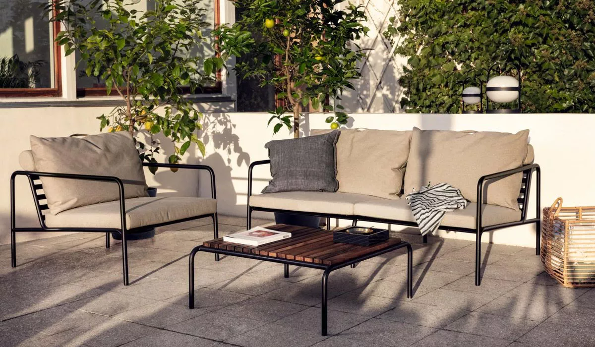 Houe Loungemöbel in Beige auf einer Terrasse mit Pflanzen im Hintergrund, bestehend aus einem Sofa, Sessel und Holztisch.
