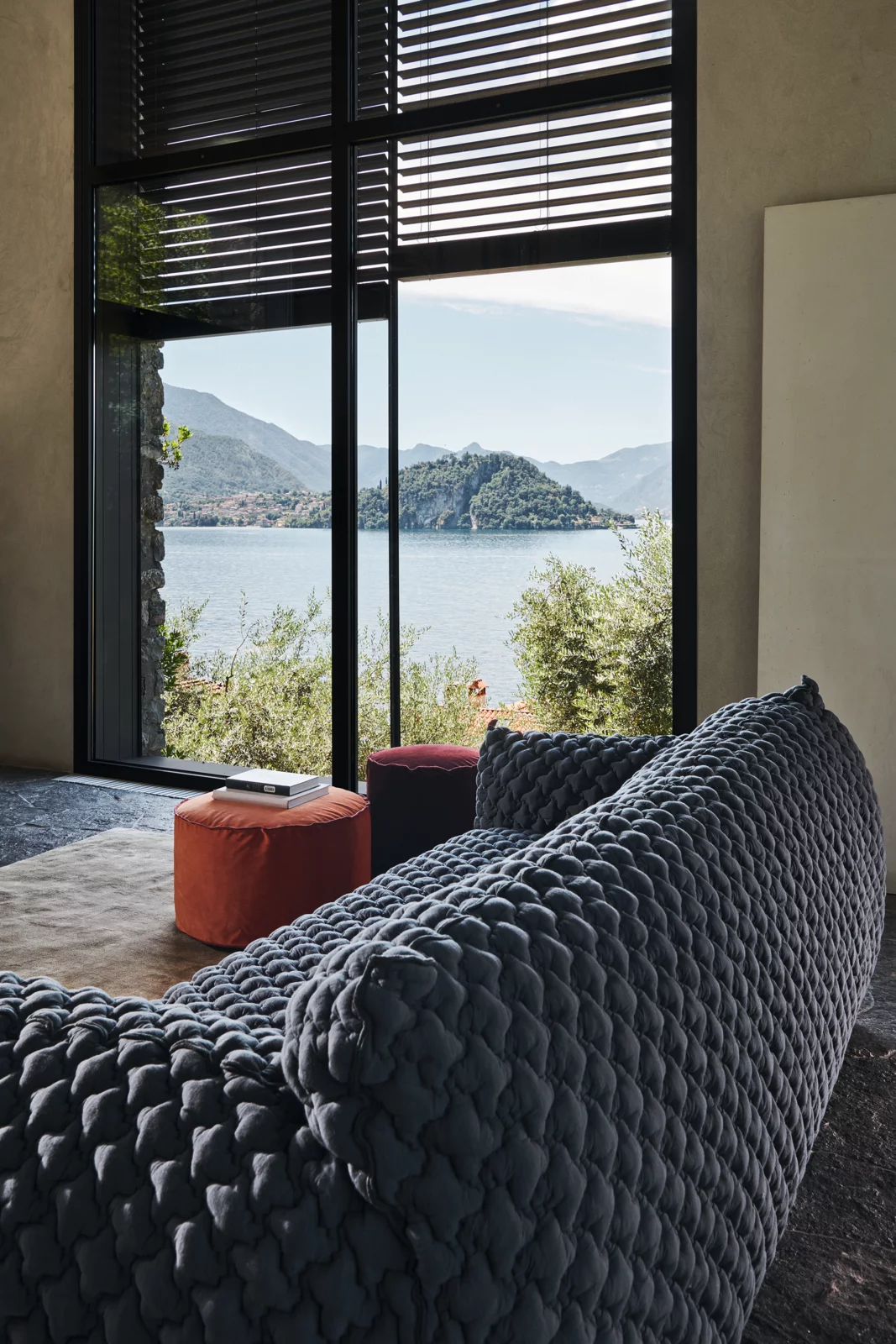 Graues Loll Next Nuvola Sofa in modernem Wohnzimmer mit Seeblick, umgeben von großen Fenstern und natürlichem Licht.