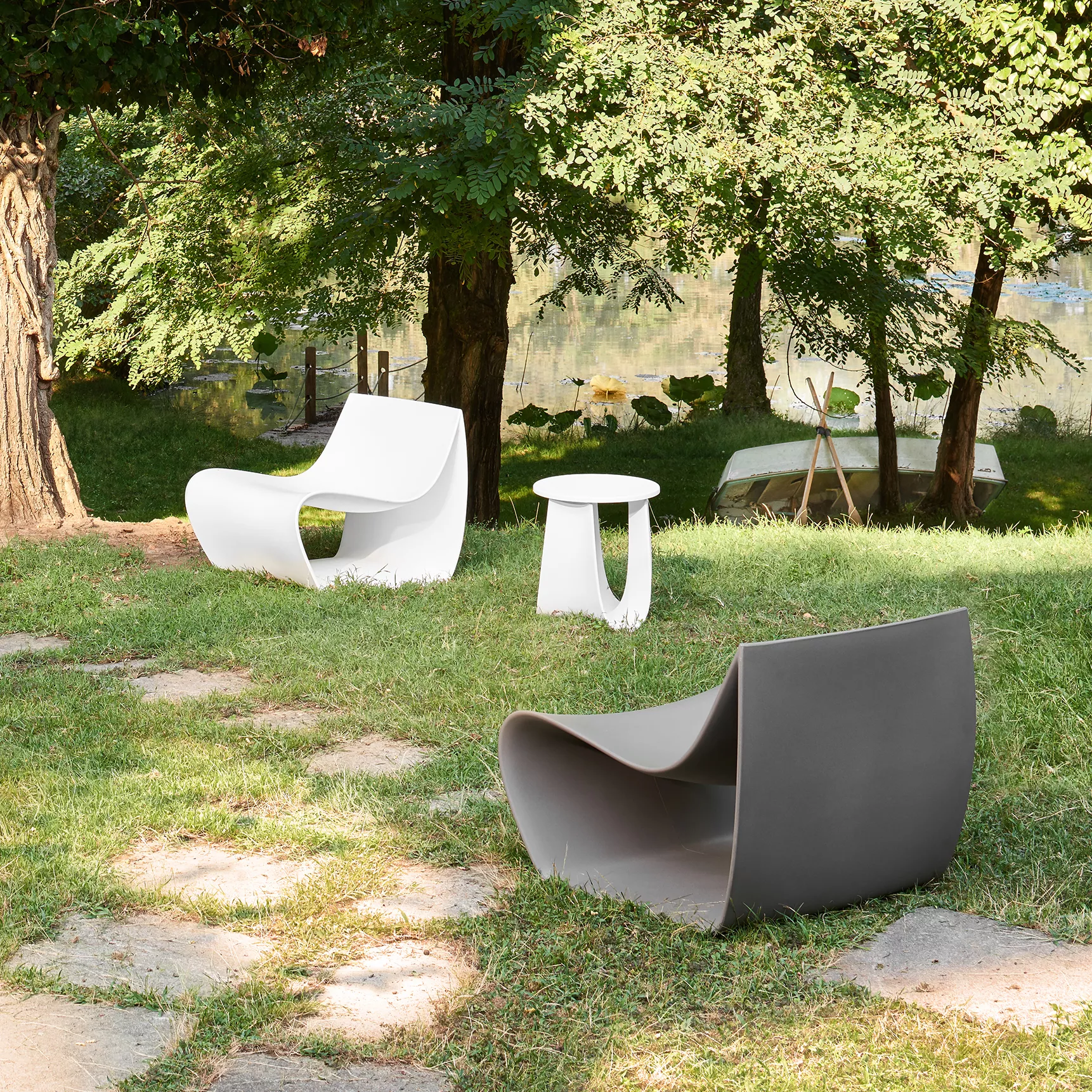 Drei MDF Italia Sign Matt Stühle und ein Tisch stehen auf einer Wiese im Freien mit Bäumen und einem See im Hintergrund.