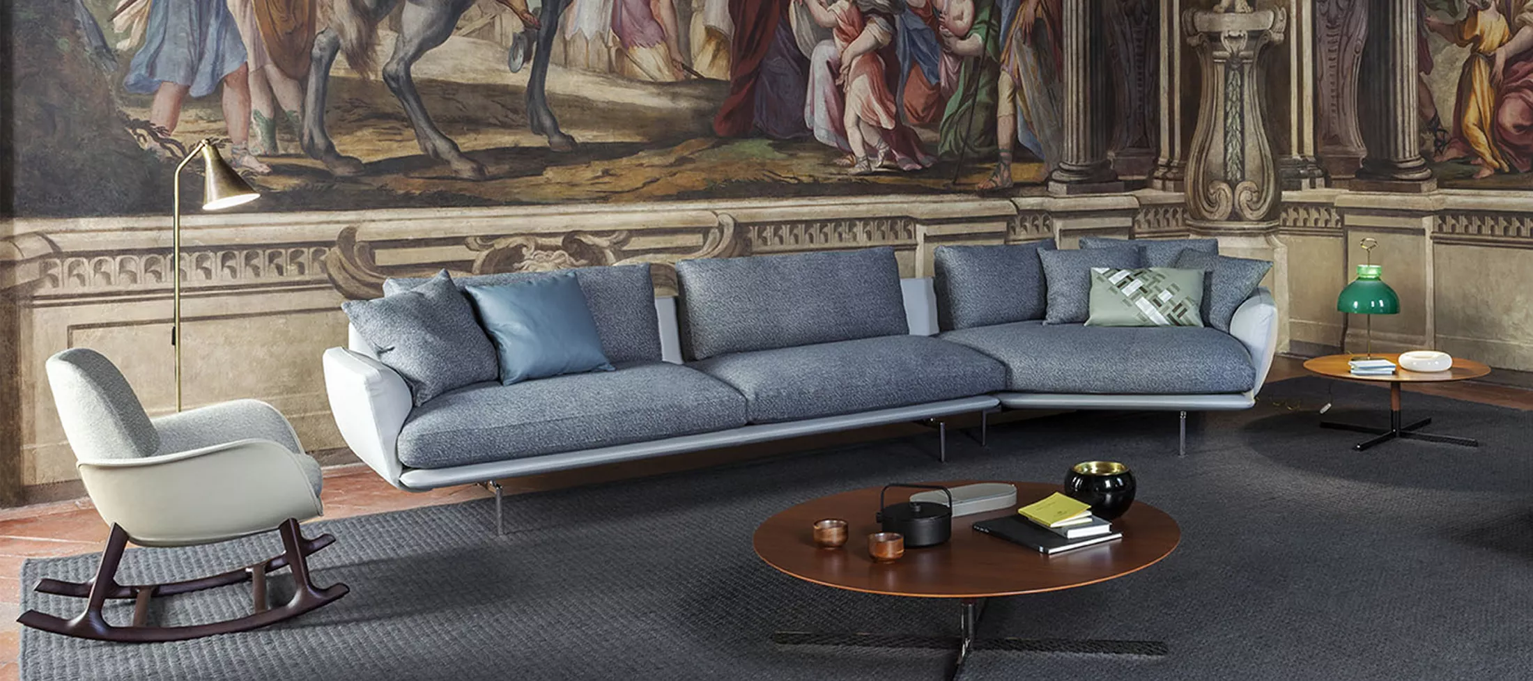 Poltrona Frau Sofa in Blau und Sessel in Cremeweiß vor einer kunstvollen Wandmalerei in einem stilvollen Wohnzimmer.