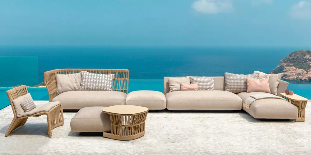 Talenti Cliff Gartenmöbel-Kollektion in Beige auf einer Terrasse mit Meerblick, bestehend aus Sofa, Sessel und Tisch, in entspannter Atmosphäre.