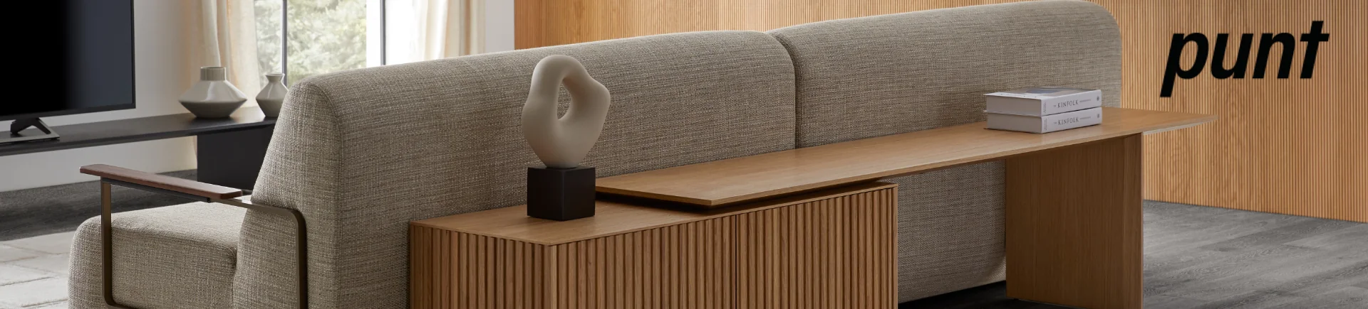 Gemütliches Wohnzimmer mit beigem Punt-Sofa, Holztisch und moderner Dekoration vor einem Holzhintergrund.