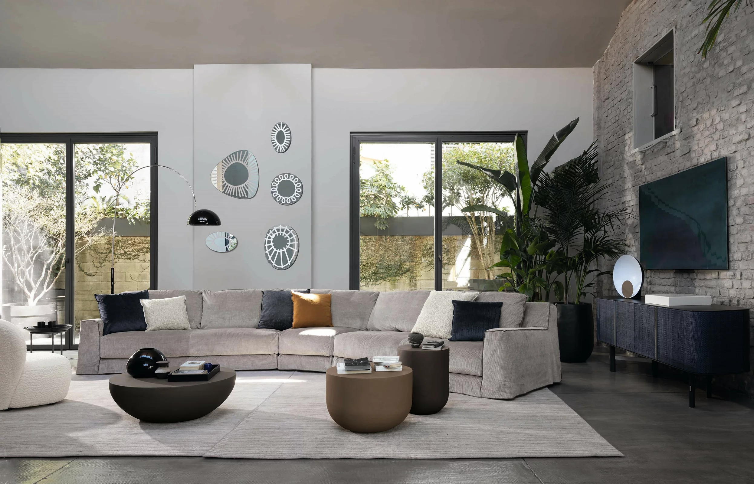 Gervasoni Sofa in modern Wohnzimmer mit grauem Sofa Couchtischen und Dekorationen an der Wand mit großen Fenstern und Pflanzen im Hintergrund