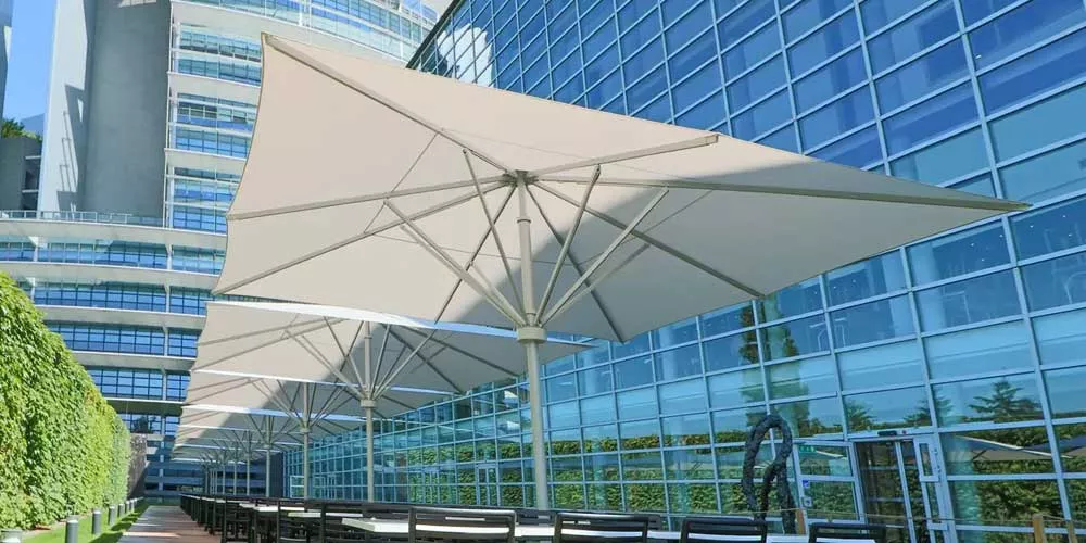 May Sonnenschirme Schattello in Beige vor einem modernen Bürogebäude, stimmungsvolles Bild mit urbanem Hintergrund.