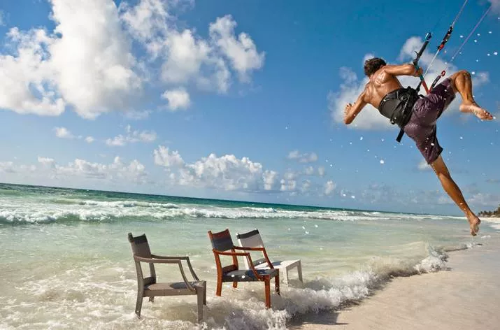 Ein Mann kitet am Strand während drei Dedon Play Essstühle in verschiedenen Farben im Wasser stehen Moodbild am Meer.